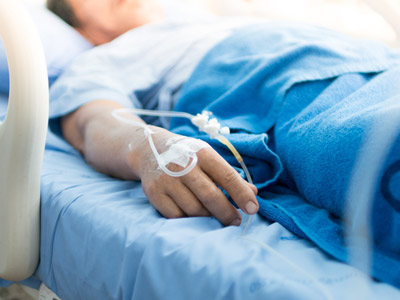 Eine Hand eines Patienten, die an ein intravenöses Infusionssystem angeschlossen ist, liegt auf einem Bett mit blauer Bettwäsche.